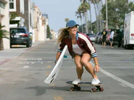 Girl holding a surfboard riding a Yow surfskate complete